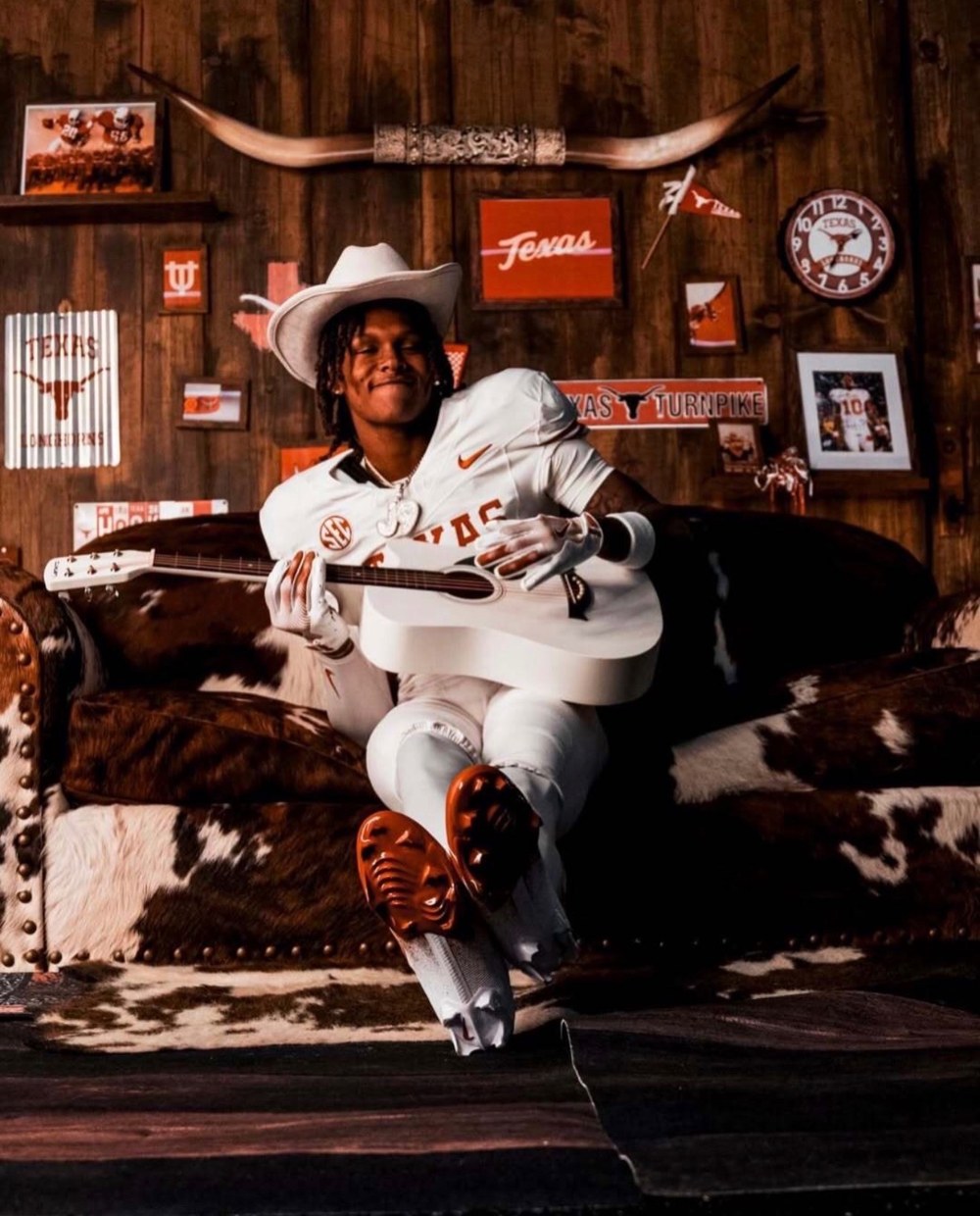 John Meredith III in a Texas Longhorns uniform and cowboy hat, holding a guitar during his Texas visit